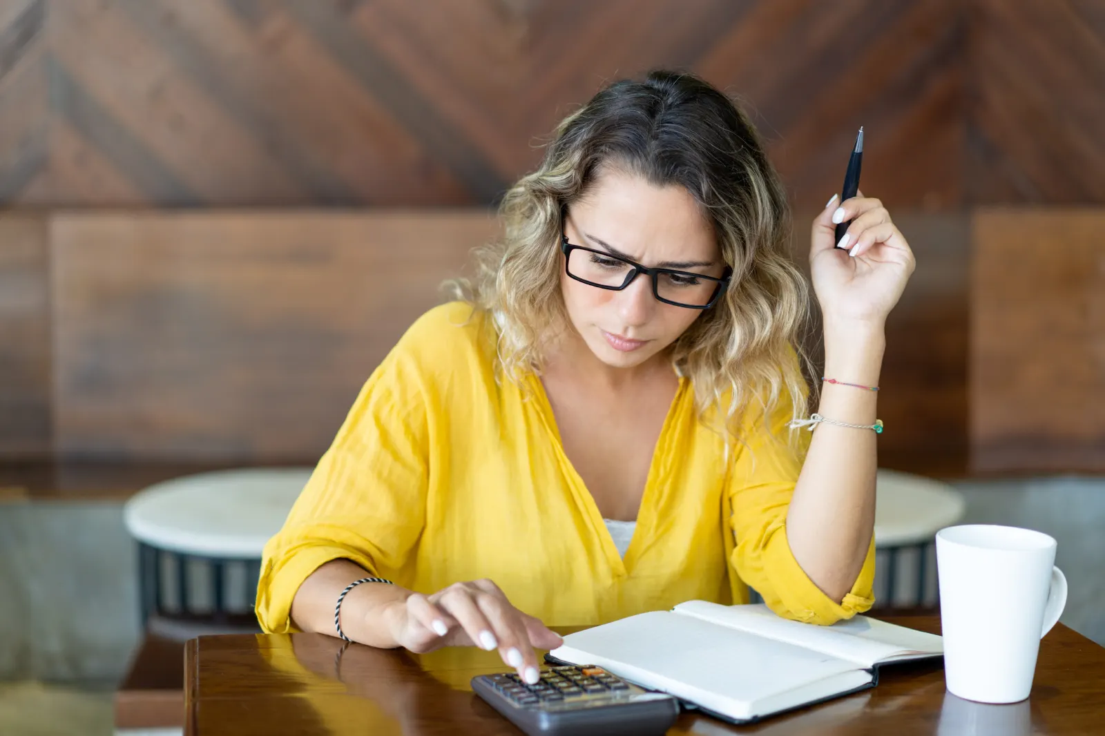 Mujer con gafas concentrada usando una calculadora y revisando un cuaderno