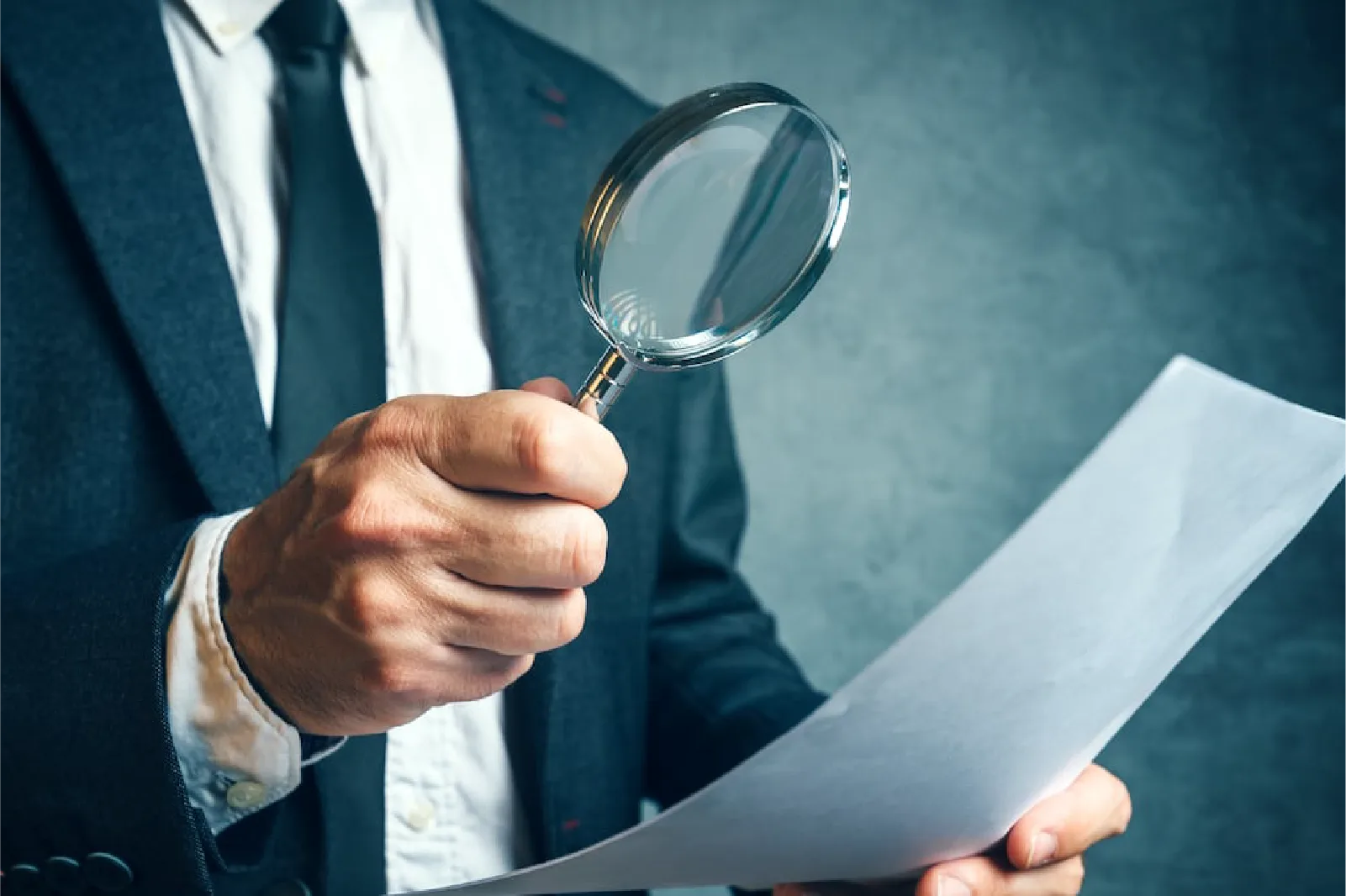 Persona con traje de negocios examinando un documento con una lupa